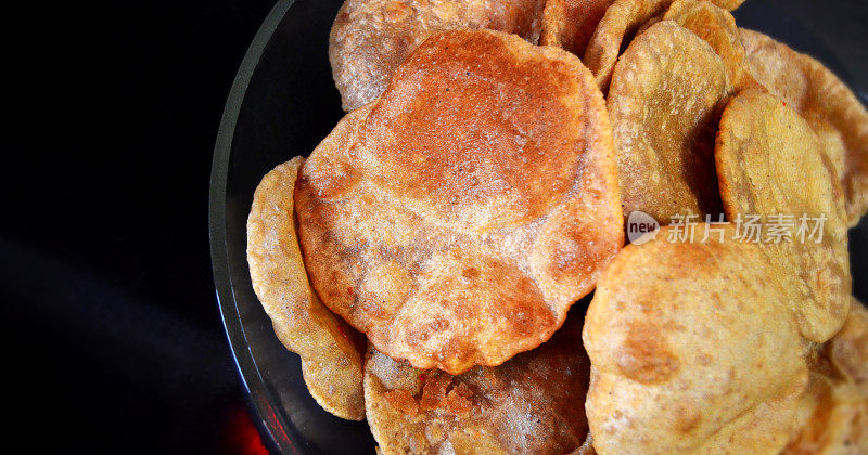 一堆或一堆煮熟的食物，用全麦面粉puris luchi或poori bhaji，油炸的扁平面包放在玻璃盘或碗里，黑色背景，用于烹饪，膳食或与食物相关的背景，带有复制空间的壁纸